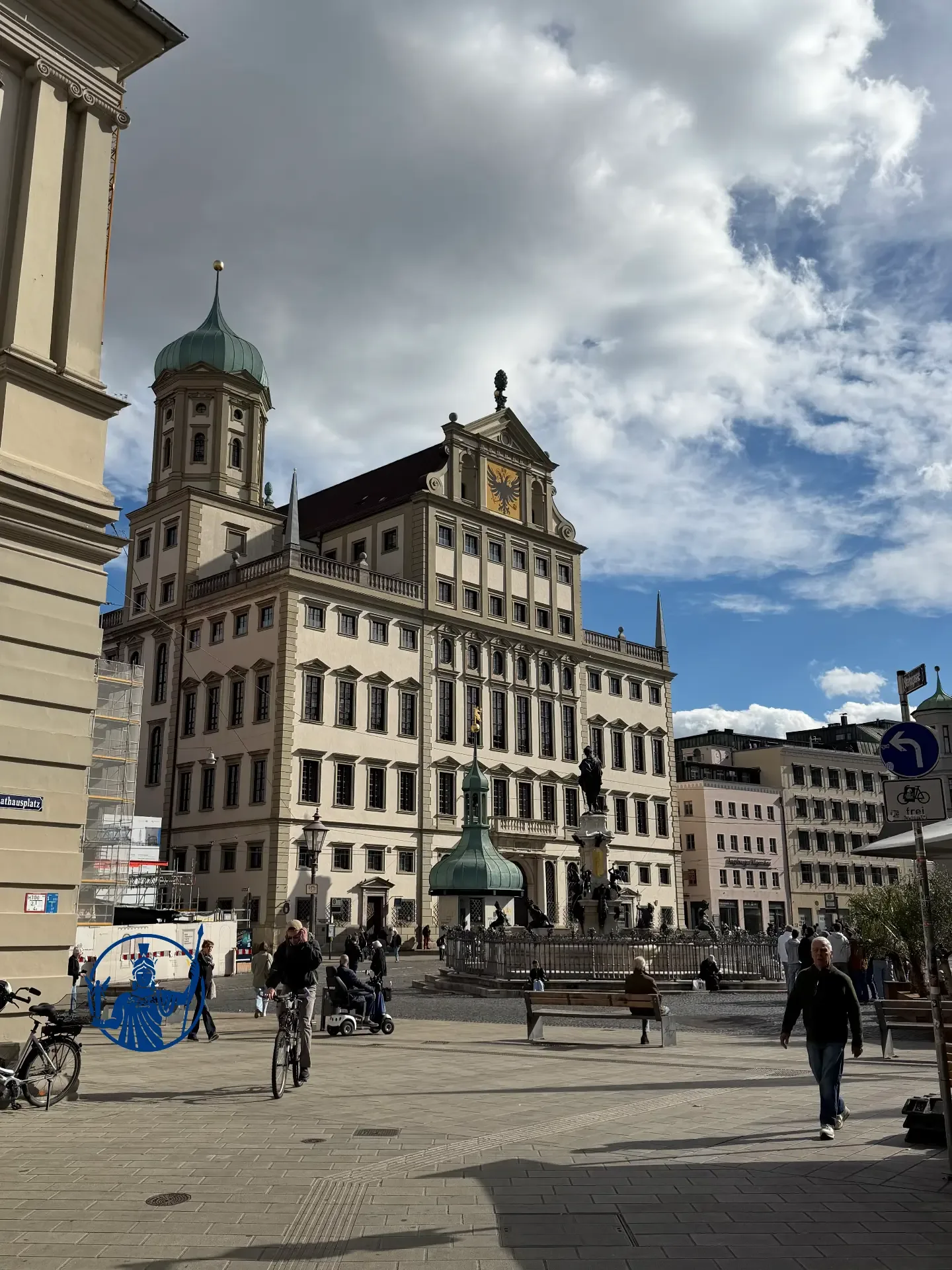 Schrägansicht des Augsburger Rathauses über den Rathausplatz mit Augustusbrunnen, Passanten und einem Radfahrer