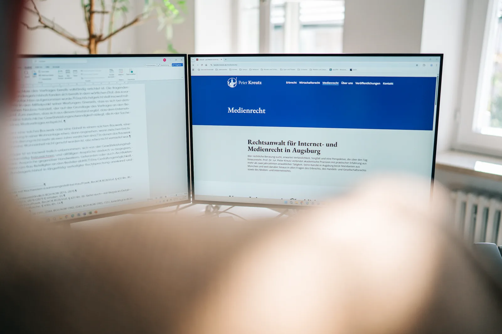 Arbeitsplatz mit zwei Bildschirmen und juristischen Texten